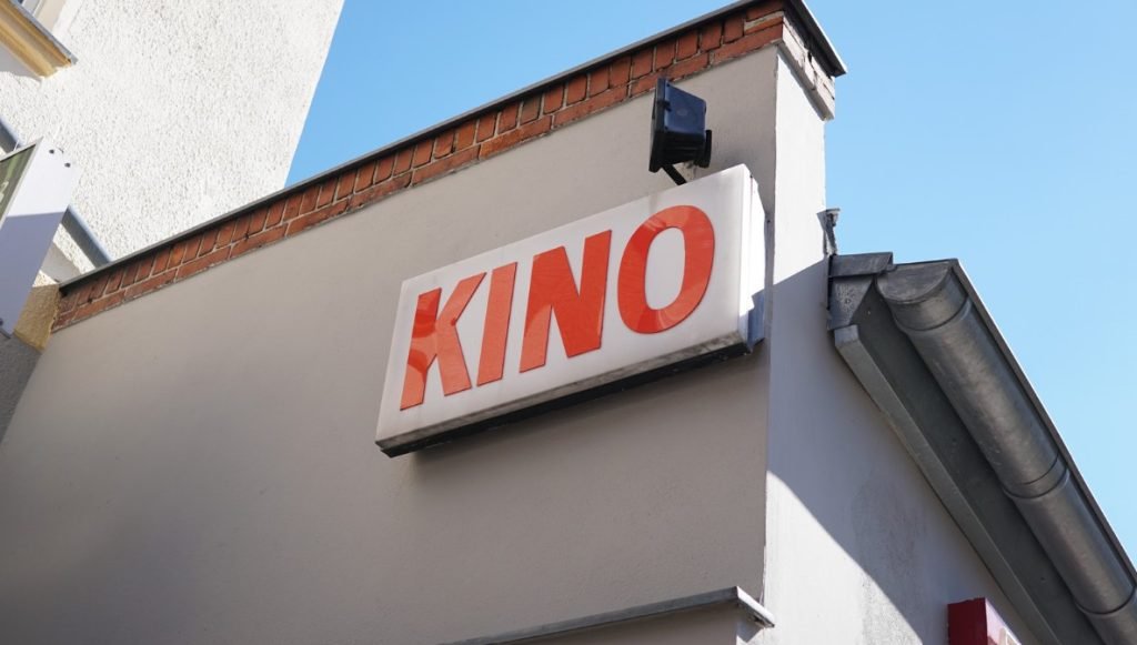 Blick von hinten durch einen historischen Kinosaal auf die beleuchtete Leinwand